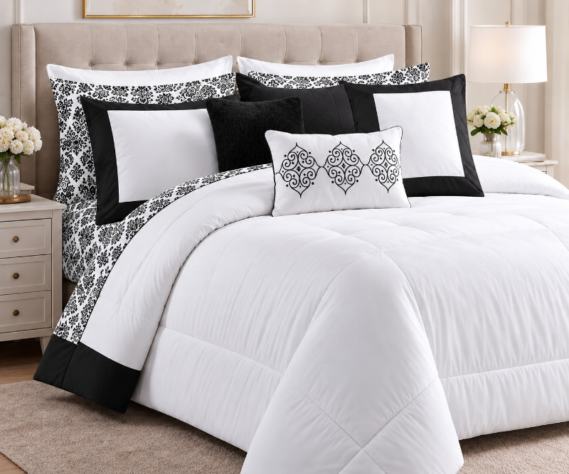 A neatly made bed dressed in a white comforter set with black and white patterned pillows and shams, styled in a bright bedroom with a tufted headboard, bedside tables, flowers, and a lamp.
